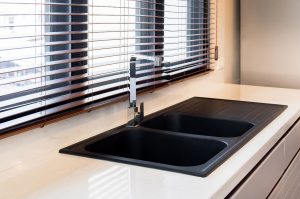 Modern kitchen interior in the city apartment. White marble,quartz counter top kitchen with black sink and faucet,wooden blind sunlight through the windows in the city clean and luxury design.